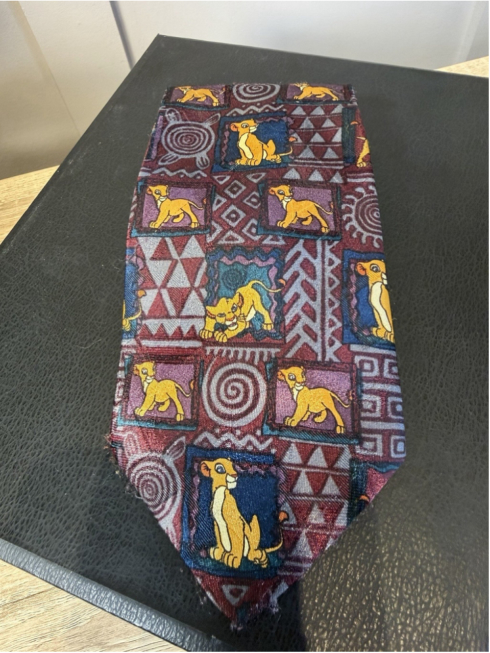 This Disney The Lion King necktie features a vibrant burgundy and blue Simba